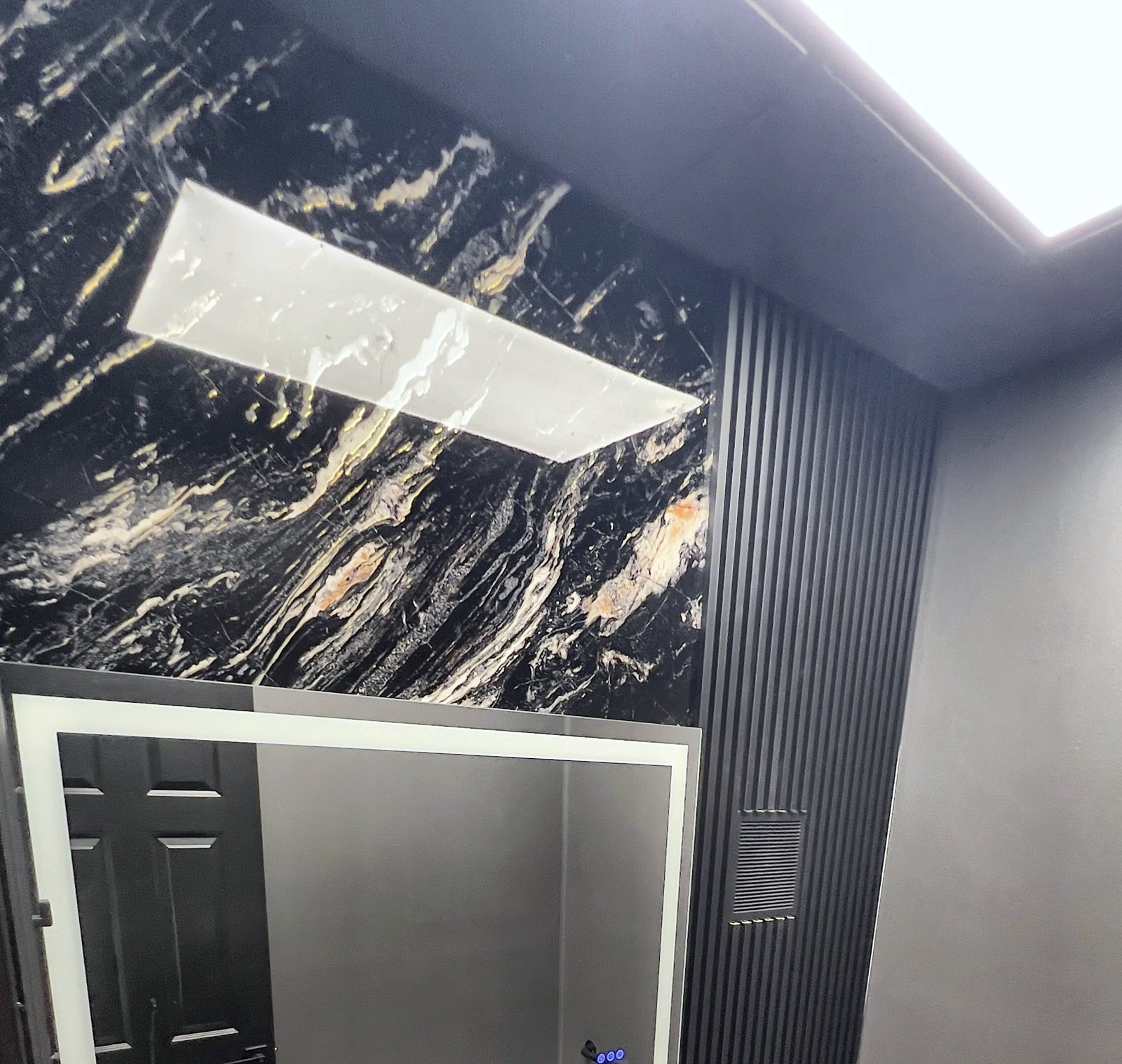 After: commercial restroom remodel with black marble slab wall, slat-wall accent and LED mirror — Lake Mary FL